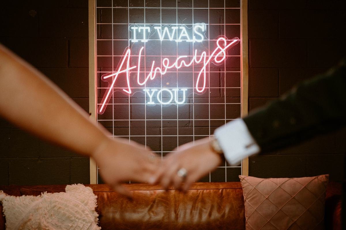 It Was Always You neon sign behind a couple holding hands