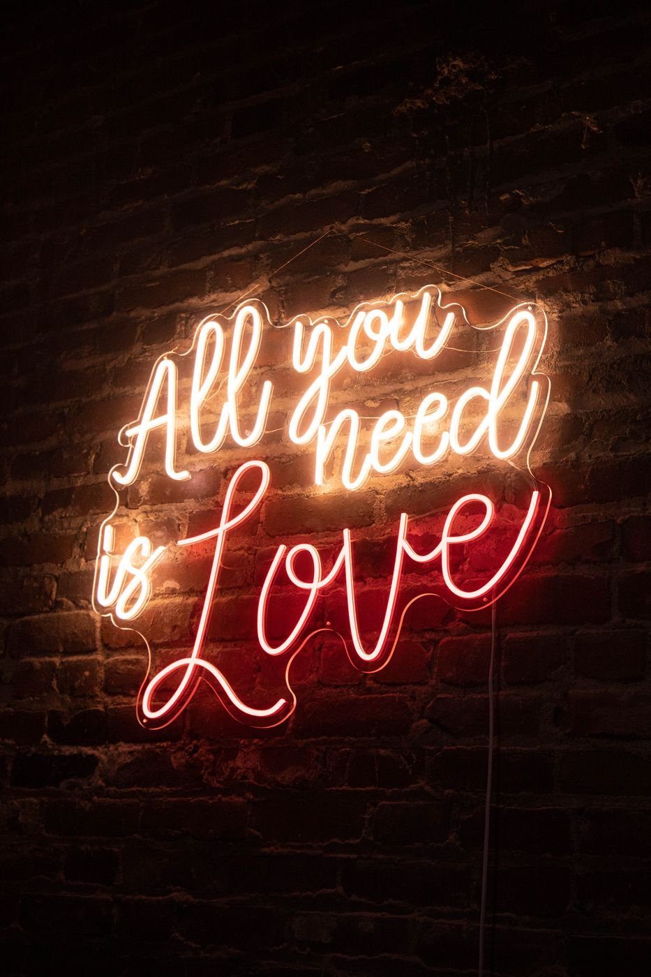 All You Need Is Love two-tone neon sign on a brick wall