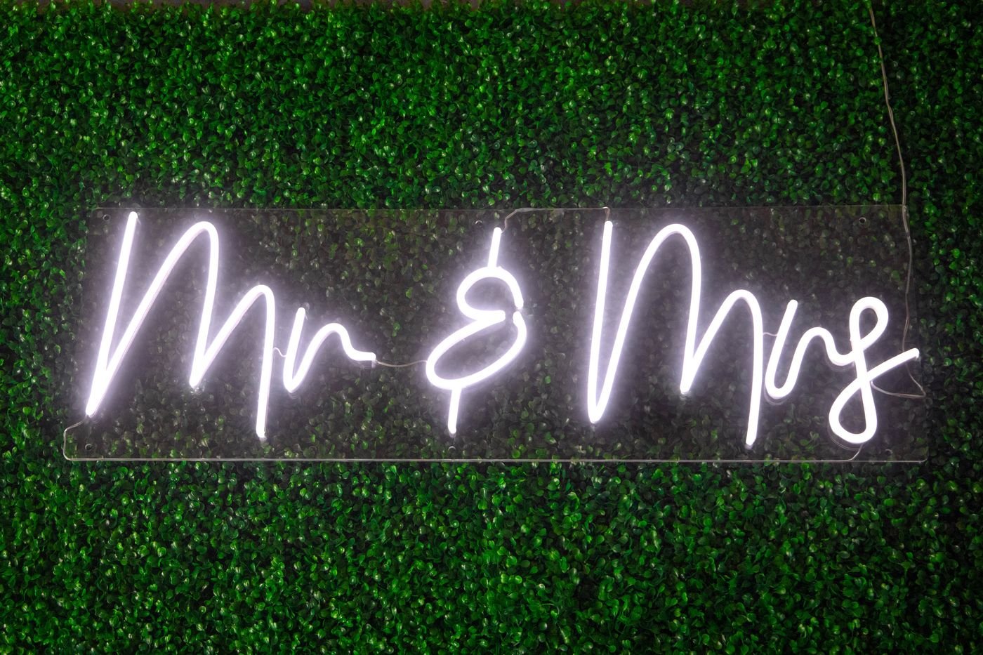 Mr and Mrs script neon sign on a greenery wall